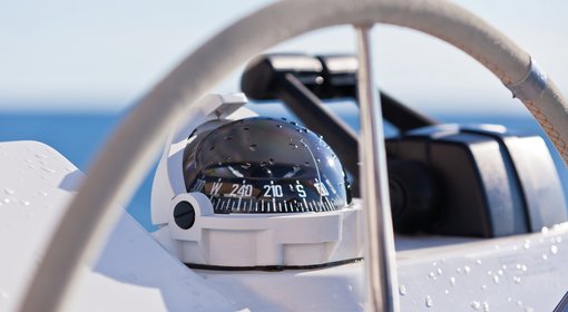 Zeigt einen Kompass, Teile eines Steuerrads sowie den Gashebel eines Bootes. 