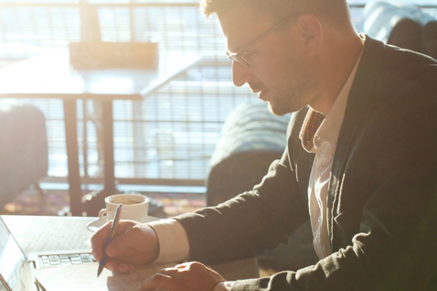 Person sitzt am Laptop und schreibt etwas auf einen Block.