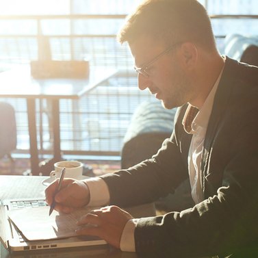 Person sitzt am Laptop und schreibt etwas auf einen Block.