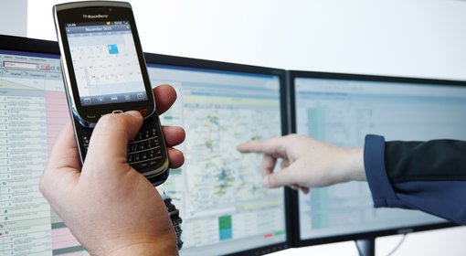 Eine Person hält ein Handy in der Hand und zeigt auf einen Computer-Bildschirm.