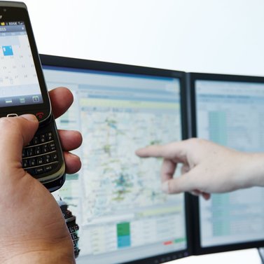 Eine Person hält ein Handy in der Hand und zeigt auf einen Computer-Bildschirm.