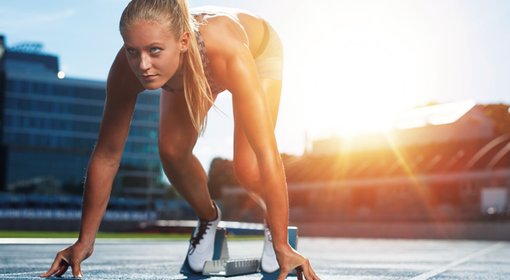 Eine  Frau in einem Startblock auf einer Tartanbahn. 