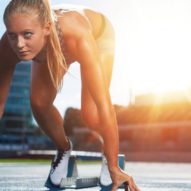 Eine  Frau in einem Startblock auf einer Tartanbahn. 